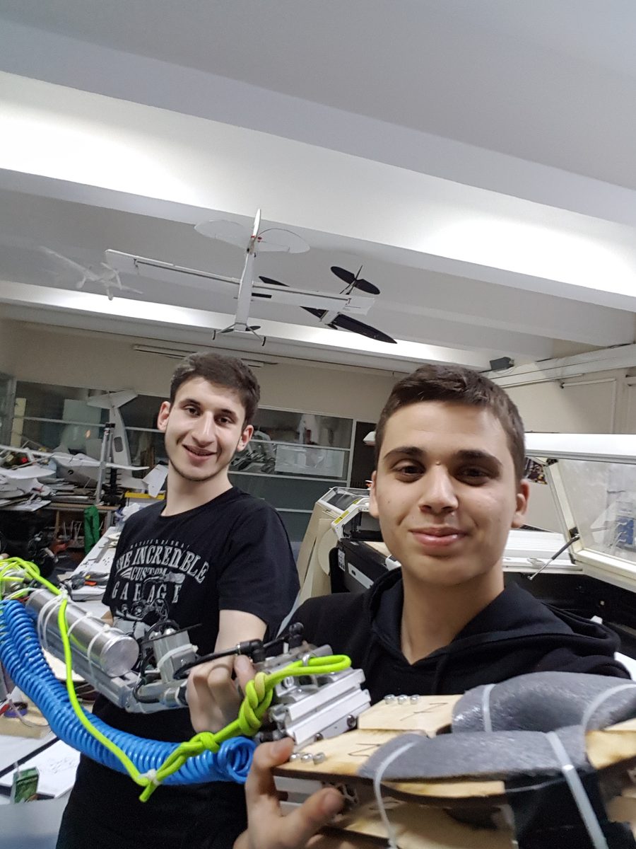 Onat Cakici and a teammate holding the telescoping pneumatic rescue arm and soft gripper they built